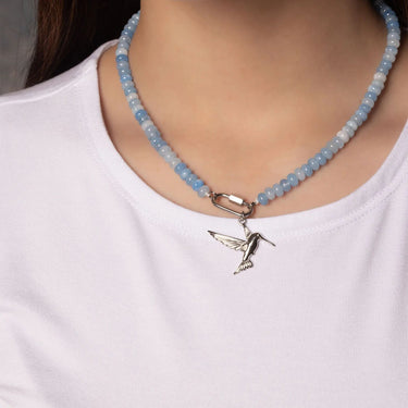 Necklace with a blue beaded chain and a silver hummingbird pendant on a white shirt.