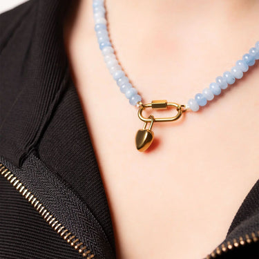 Necklace with a gold lock charm on a person wearing a black garment.