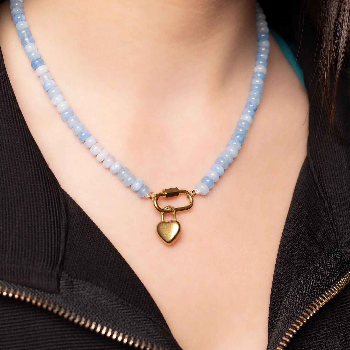 Necklace with blue beads and a gold heart lock clasp worn by a person.