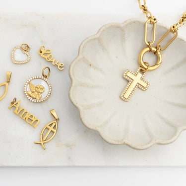 Gold pendants including a cross, fish symbol, and 'Amen' on a marble surface.
