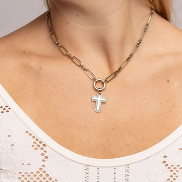 Necklace with a cross pendant worn by a person in a white top.