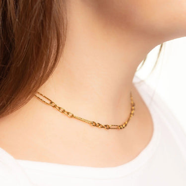 Gold chain necklace worn by a person on a plain background