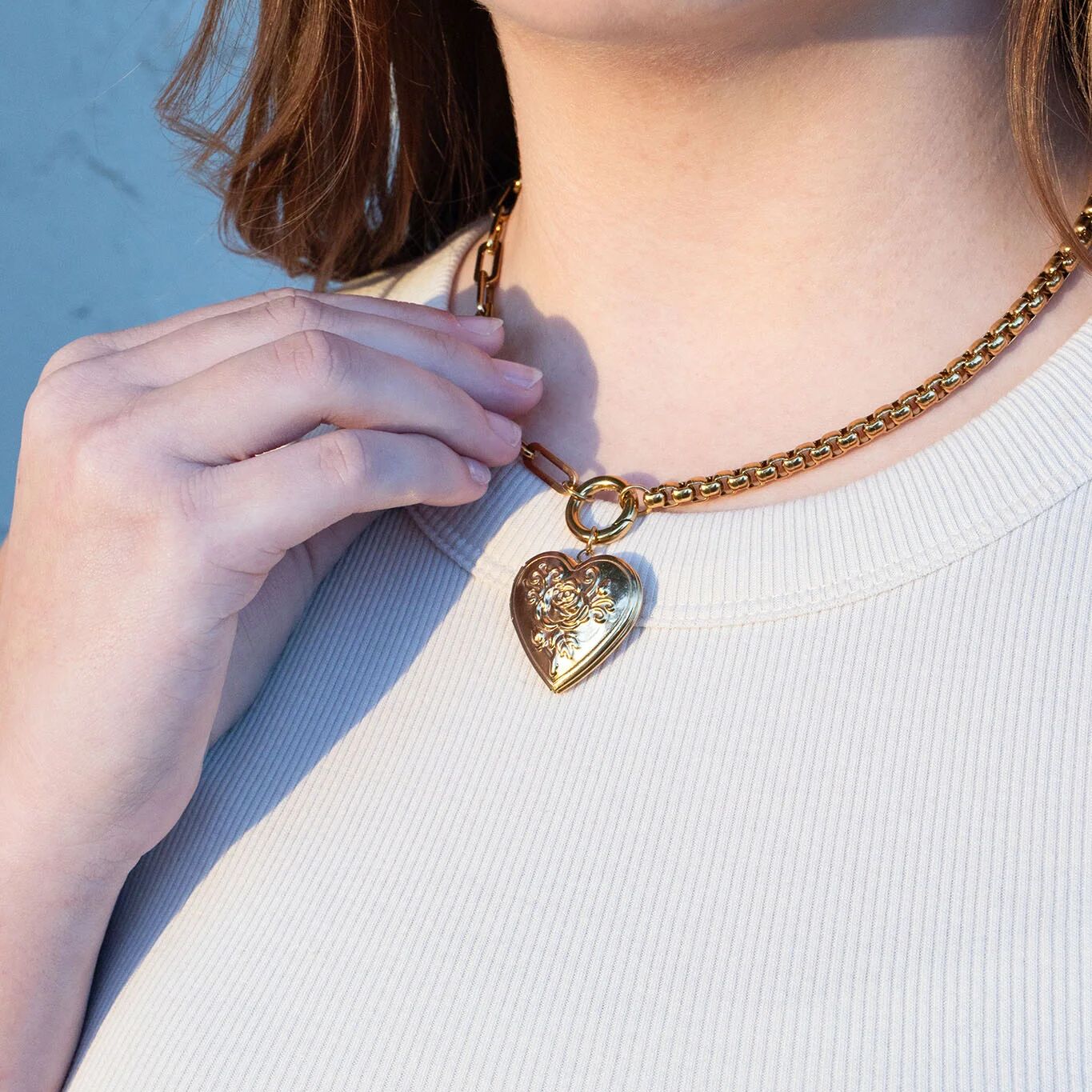 Person wearing a gold necklace with a heart-shaped pendant