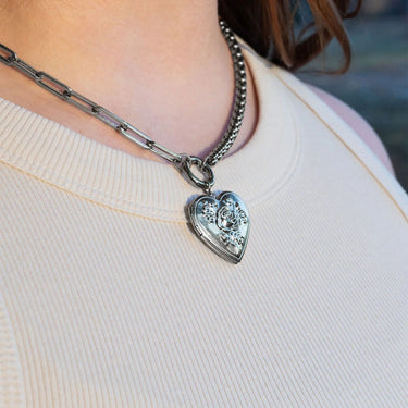 Heart-shaped silver pendant on a chain necklace worn by a person.