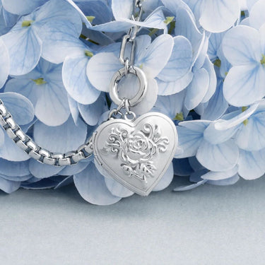 Silver heart-shaped locket with floral design on a blue hydrangea flower background