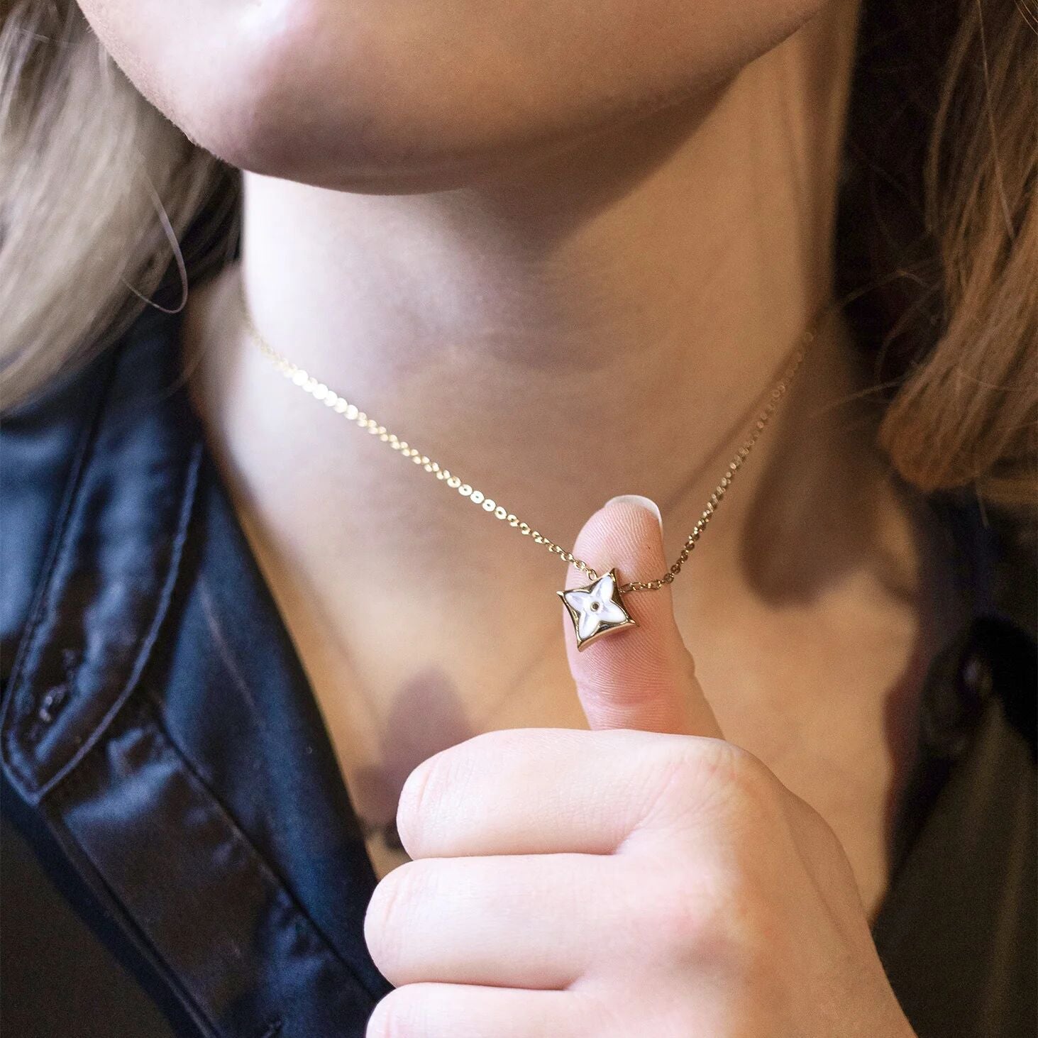 Person wearing a gold necklace with a star pendant, pointing to it.