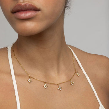 Close-up of a person wearing a gold necklace with floral pendants against a neutral background