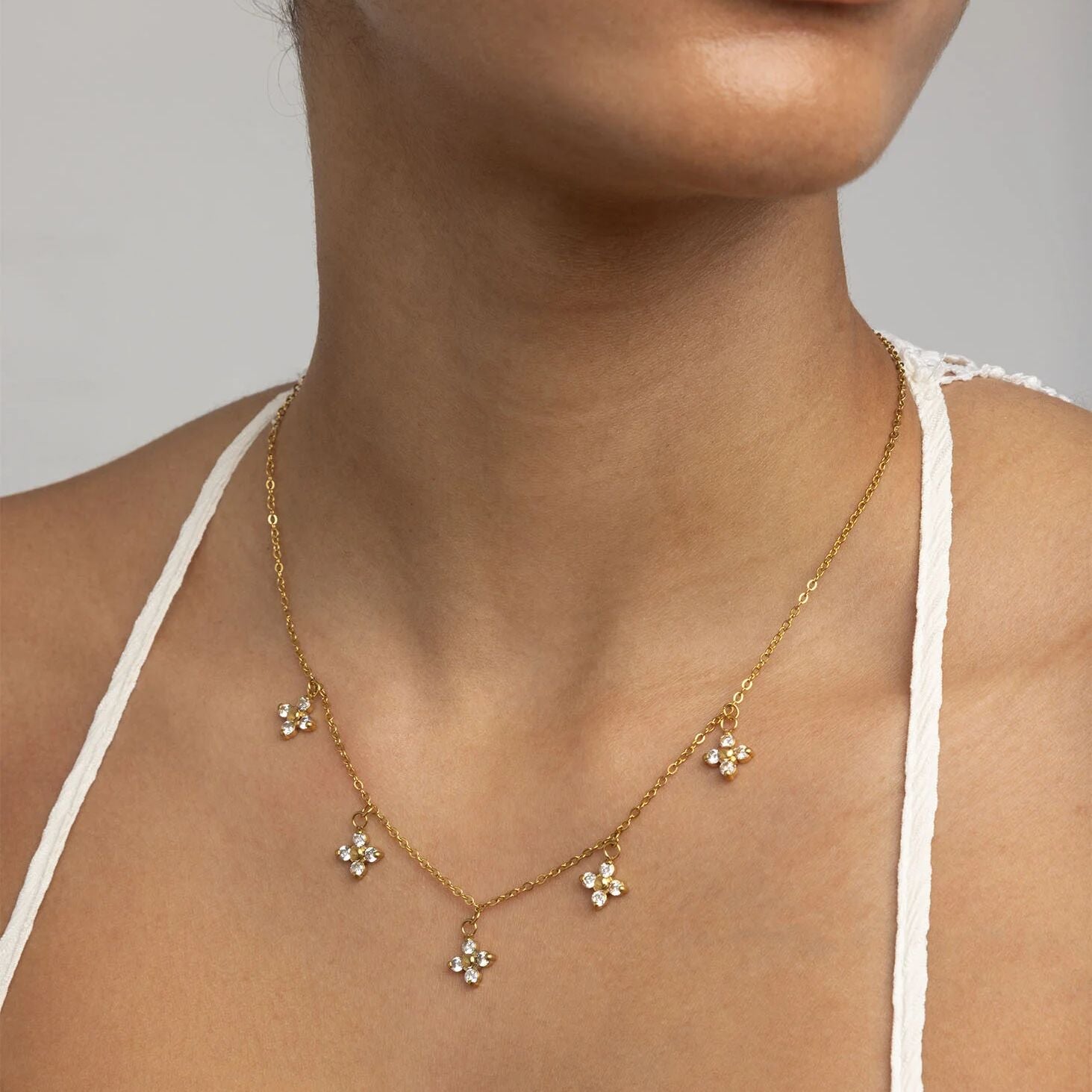 Gold necklace with floral pendants on a person wearing a white top against a neutral background
