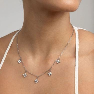 Silver necklace with floral pendants on a person wearing a white top.