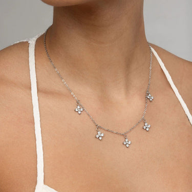 Silver necklace with floral pendants on a person wearing a white tank top.