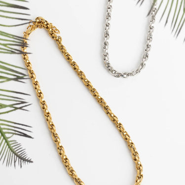 Gold and silver chain necklaces on a white background with green leaves.