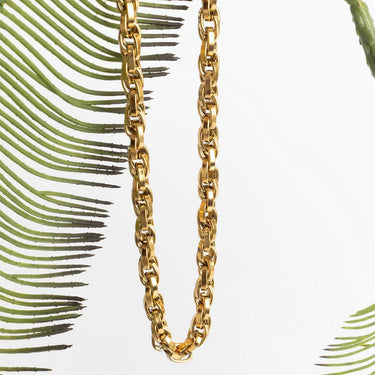 Gold chain necklace against a white background with green leaves
