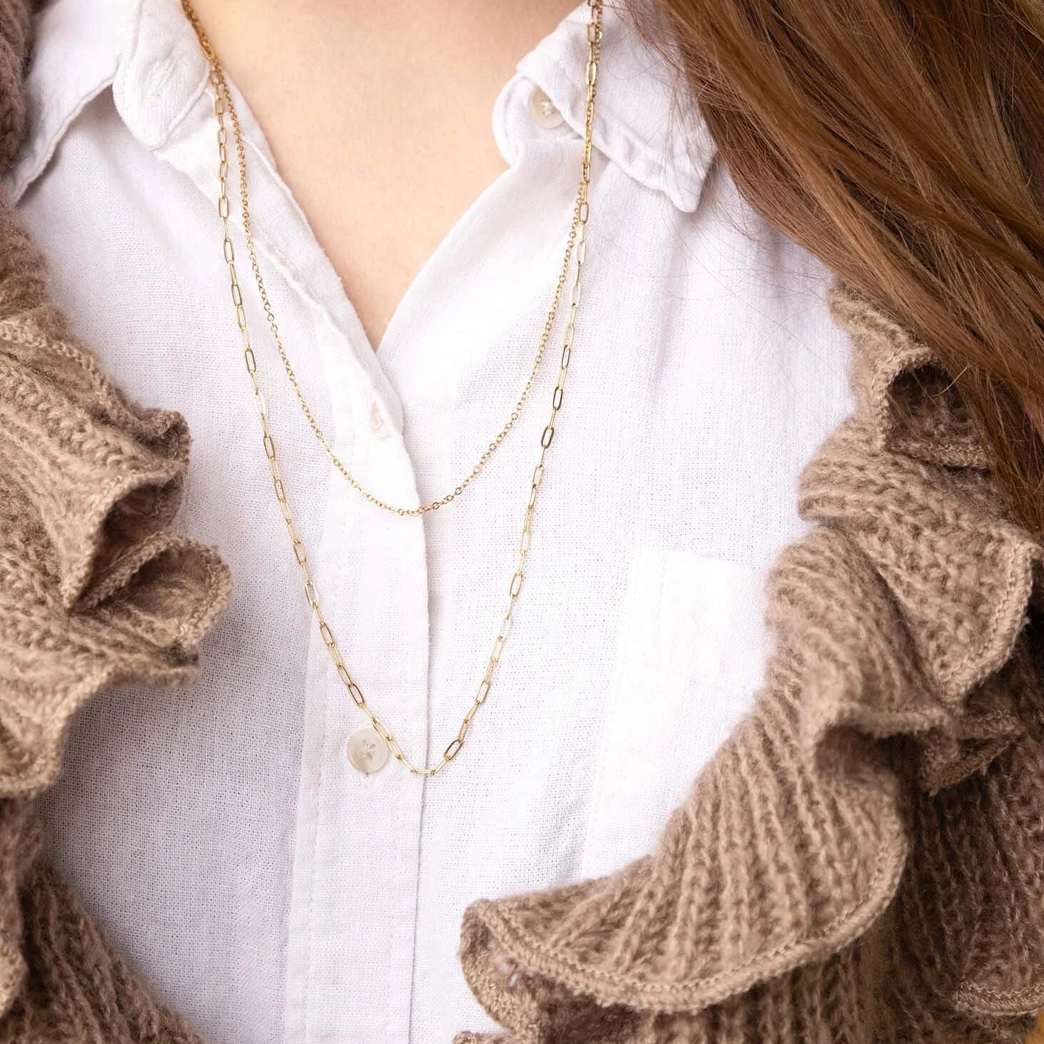 Close-up of a person wearing a white shirt with ruffled sleeves and gold necklaces.