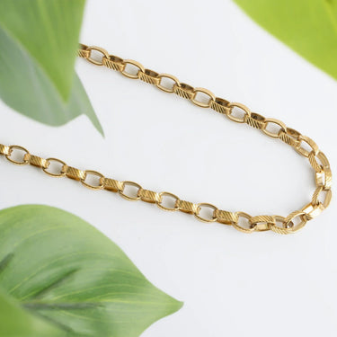 Gold chain necklace on a white background with green leaves
