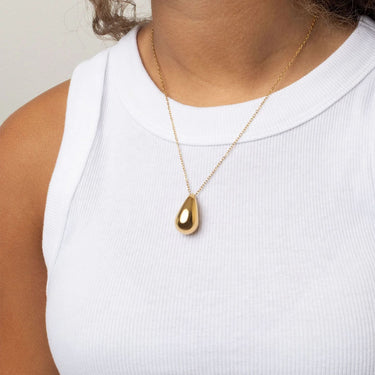Gold teardrop necklace on a person wearing a white top against a neutral background