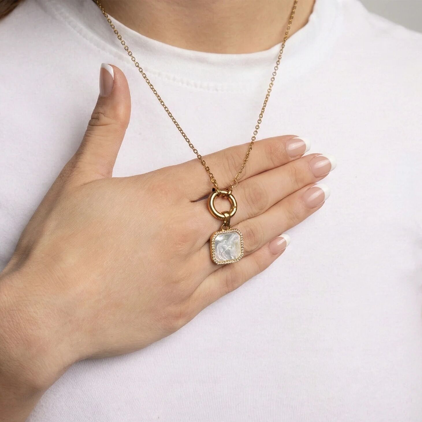 Gold necklace with a pendant held by a hand against a white background