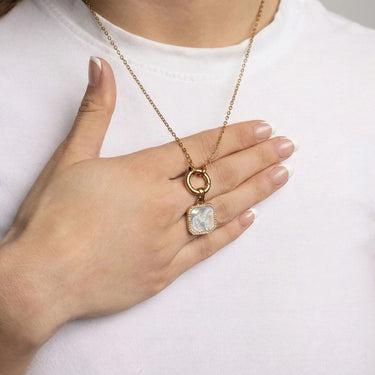 Gold necklace with a pendant held by a hand against a white background