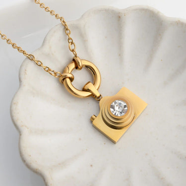 Gold camera-shaped pendant with a diamond on a marble surface