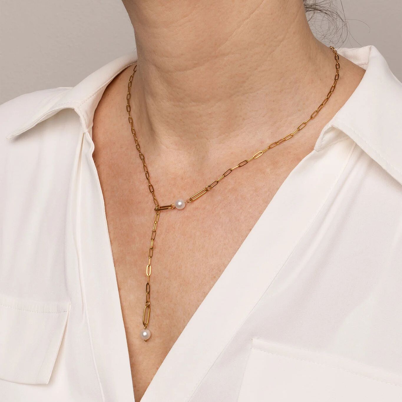 Gold necklace with pearls worn by a person in a white shirt against a neutral background
