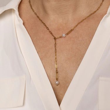 Gold necklace with pearl drops worn by a person in a white blouse.