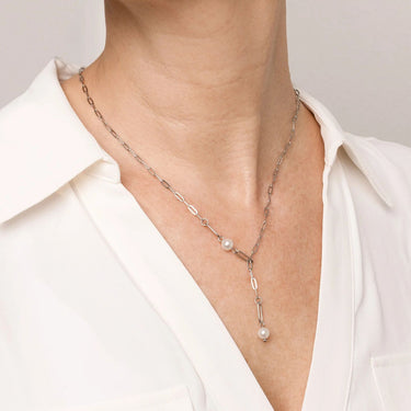 Necklace with pearl pendant worn by a person in a white shirt against a neutral background