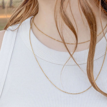 Close-up of a person wearing a delicate gold necklace with a blurred background
