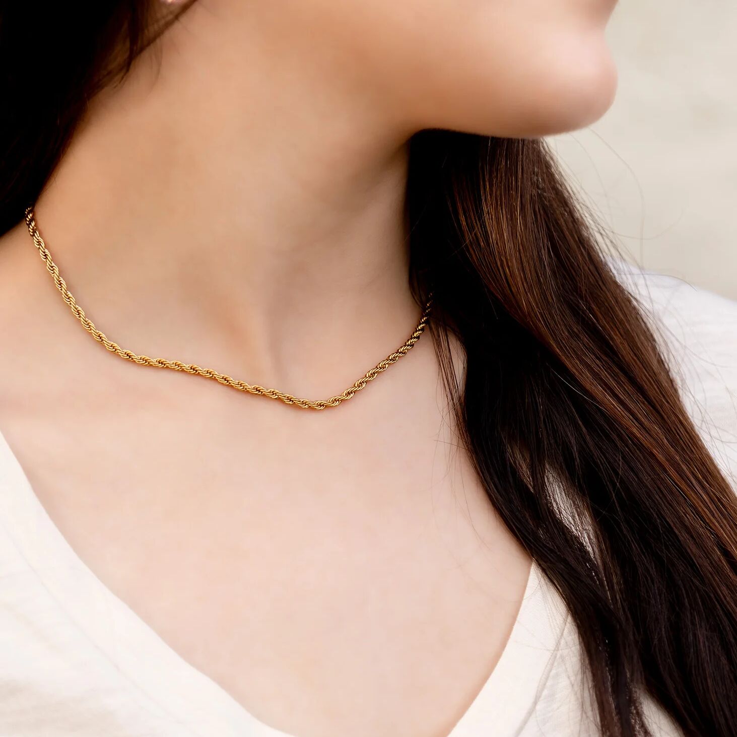Gold necklace worn by a person with a neutral background