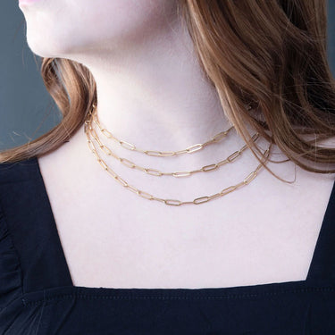Gold chain necklace on a person wearing a black top against a gray background