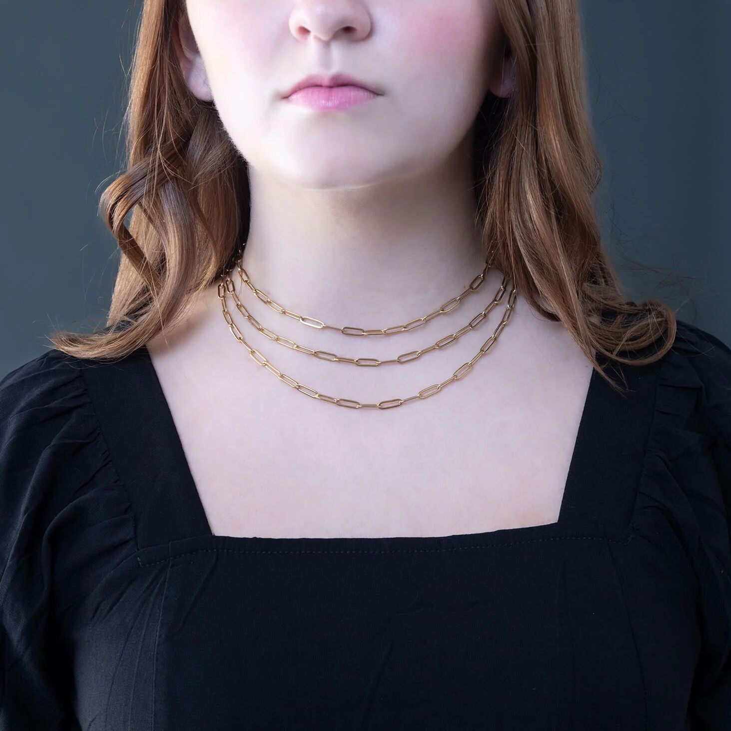 Person wearing a gold chain necklace against a dark background