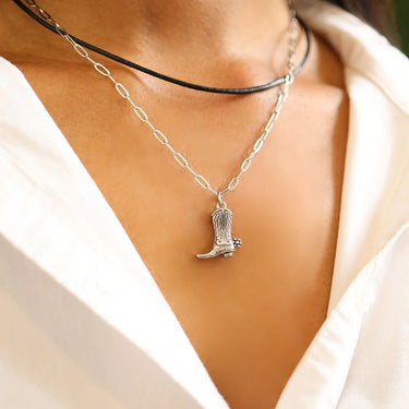 Silver necklace with a cowboy boot pendant on a person wearing a white top.