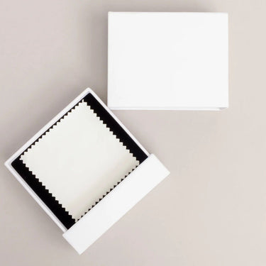 White jewelry box with open cover displaying dust cloth on a beige background