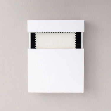 White jewelry box with cover  slightly slid up displaying dust cloth on a beige background