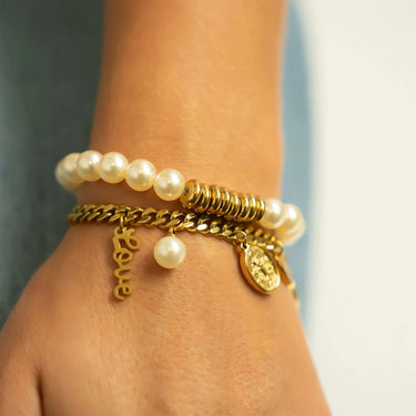 Close-up of a wrist wearing multiple gold and pearl bracelets against a neutral background