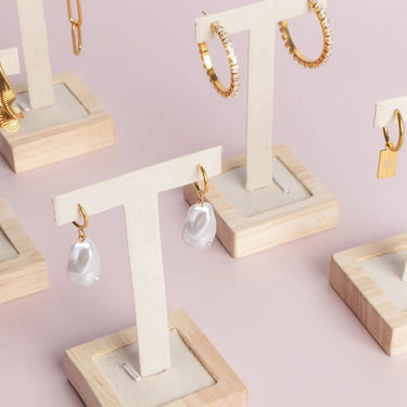 Gold and pearl earrings on wooden display stands against a light pink background