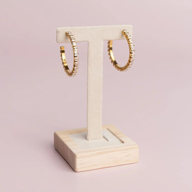Gold hoop earrings on a wooden stand against a pink background