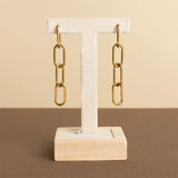 Gold chain earrings on a wooden stand against a beige background