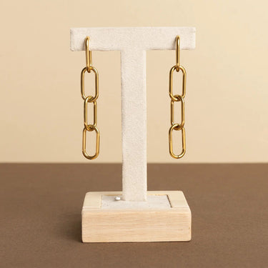 Gold chain earrings on a wooden stand against a beige background