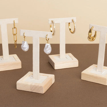Set of gold and pearl earrings on wooden stands against a beige background