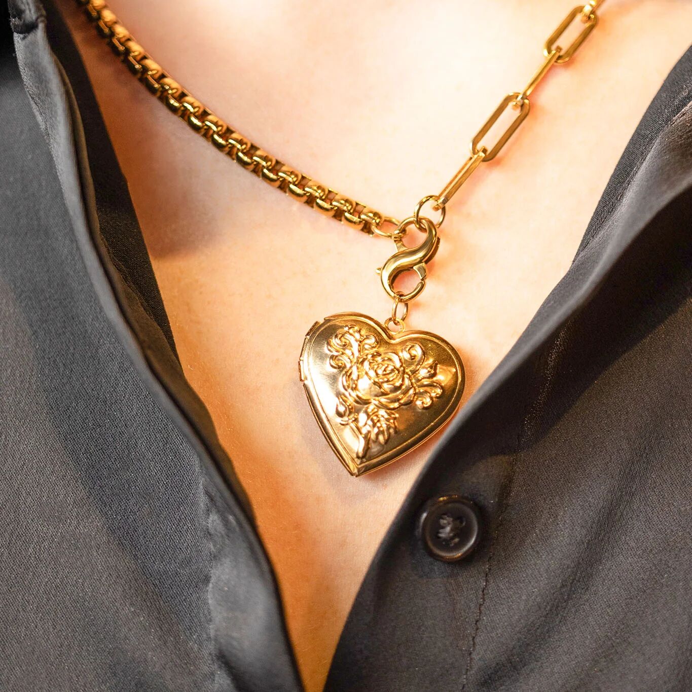 Gold heart-shaped necklace with intricate design worn by a person in a gray shirt.
