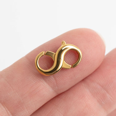 Gold infinity symbol charm on a finger against a white background