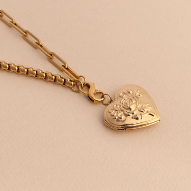 Gold heart-shaped locket with floral design on a beige background