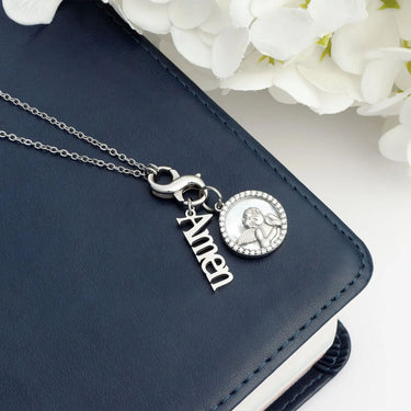 Silver necklace with 'Amen' pendant on a navy blue surface with white flowers in the background