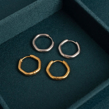Two pairs of hoop earrings, one gold and one silver, on a teal fabric surface.