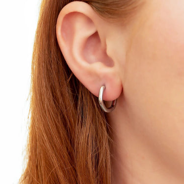 Close-up of an ear wearing a silver hoop earring with a blurred background