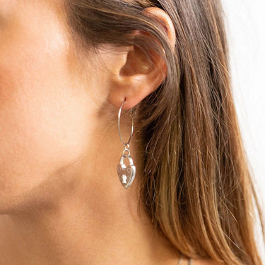 Close-up of a person wearing a silver hoop earring with a heart-shaped pendant.