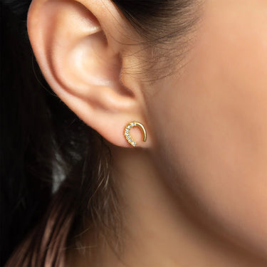 Close-up of an ear wearing a gold earring with small stones.