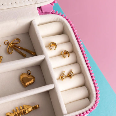 Gold jewelry including earrings and pendants in a pink and white jewelry box on a pink background