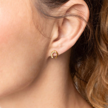 Close-up of an ear wearing a gold hoop earring with small stones.
