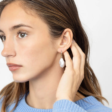 Close-up of a woman wearing pearl earrings with a plain background