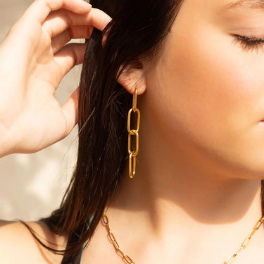 Close-up of a person wearing gold chain earrings with a neutral background
